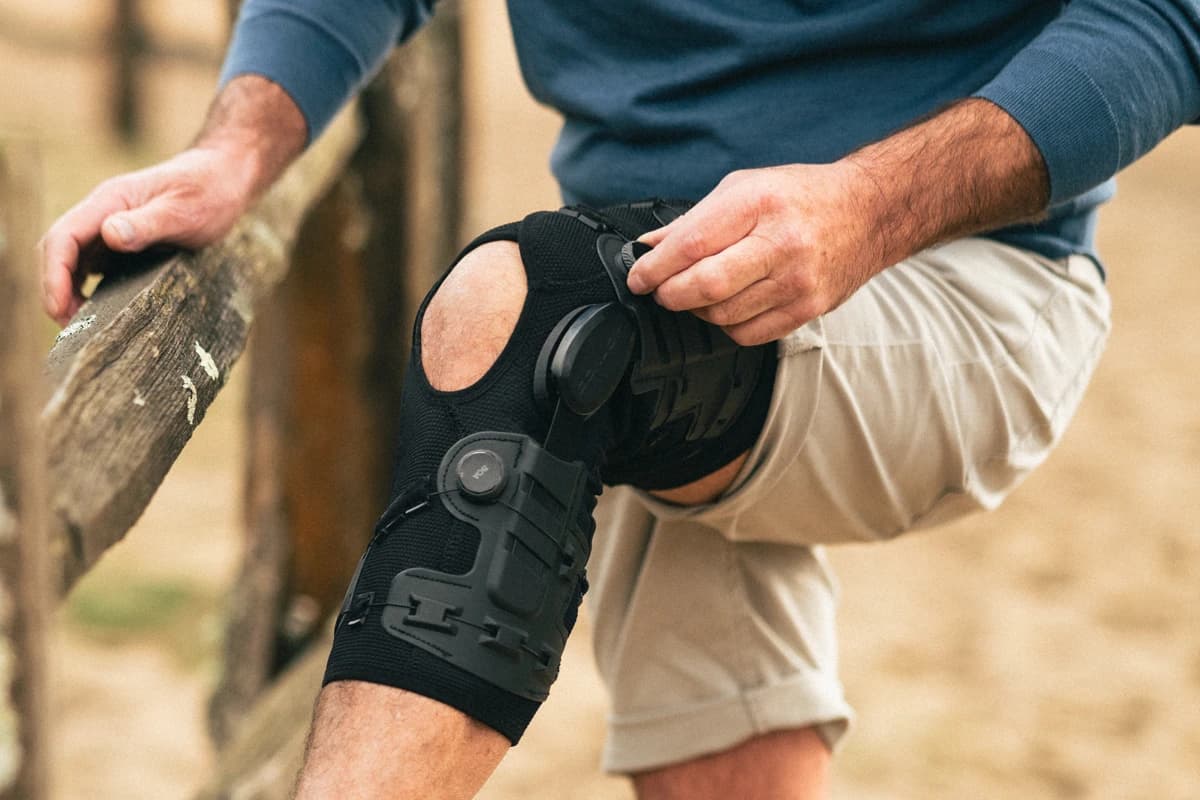 A man wearing an OA GO® brace adjusts it with the BOA® dial while being active in nature.